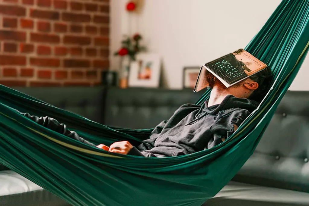 Personne allongée dans un hamac intérieur avec un livre sur le visage, symbolisant une lecture détendue et accessible, parfaite pour se remettre à lire.